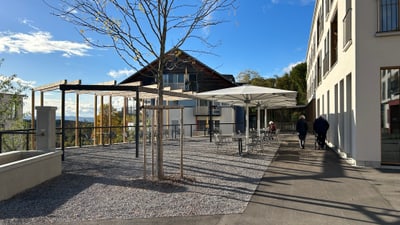 Terrasse mit Tischen, Stühlen und Sonnenschirmen bei sonnigem Wetter.