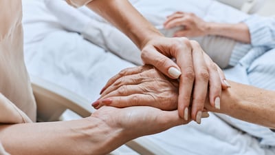 Junge Person hält die Hand einer älteren Person im Bett.