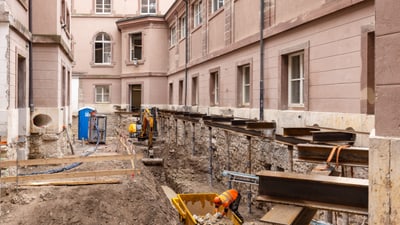 Baustelle zwischen alten Gebäuden, mit Erdarbeiten und Ausrüstung.