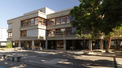 Zweistöckiges Gebäude mit grossen Fenstern und Bäumen davor.
