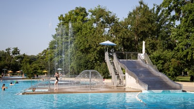 Öffentliches Freibad mit Wasserrutsche und Fontänen.