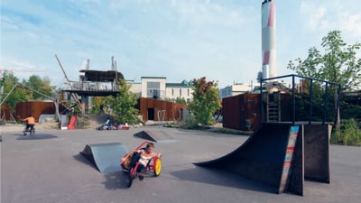 Kinder spielen auf Skatepark mit Rampen und grosser Rutsche.