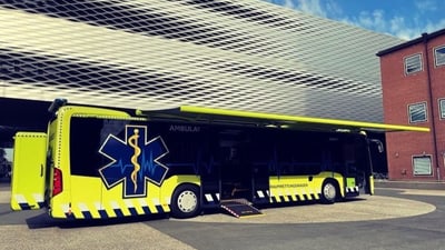 Gelber Grossraumrettungsbus vor modernem Gebäude Messe Basel.