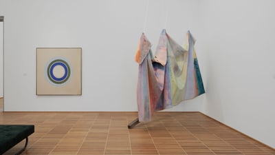 Kunstwerk im Museum mit hängendem Stoff und rundem Gemälde an der Wand.