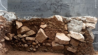 Teilweise freigelegte Mauer mit Steinen und Erde.