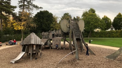 Spielplatz mit Holzklettergerüst und Rutsche, Kinder spielen.