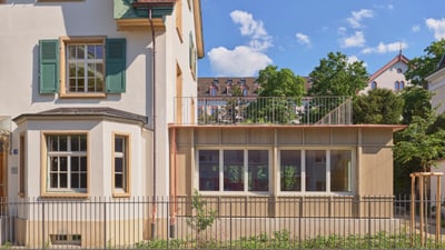 Historisches Gebäude mit modernen Anbau, Bäume im Hintergrund.