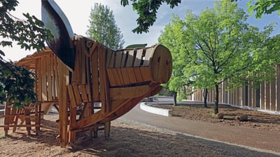 Holzspielplatz in einer Parklandschaft mit Bäumen.