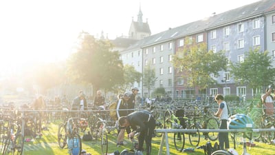 Menschen arrangieren Fahrräder auf einer Wiese bei Sonnenschein.