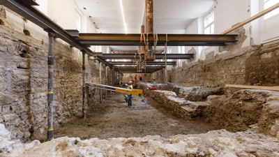 Baustelle mit Arbeitern und Maschinen in einem grossen Innenraum.