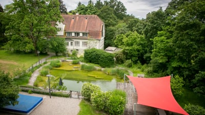 Kleines Haus mit Teich und rotem Sonnensegel im Garten.