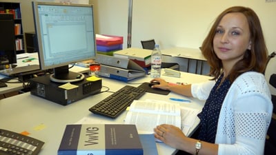 Frau am Schreibtisch im Büro mit Computer und Büchern.