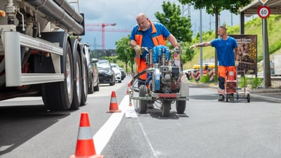 Strassenarbeiter markieren eine Fahrspur.