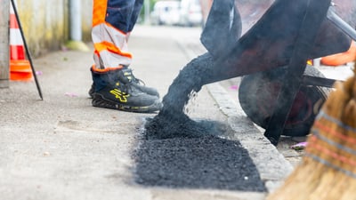 Arbeiter füllt Asphalt in ein Strassengleis.