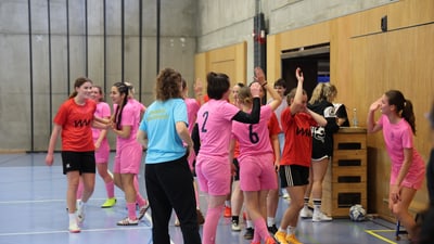 Frauenfussballteams in rosa und rot geben sich High-Fives in der Sporthalle.