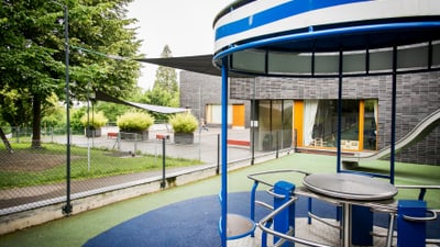 Spielplatz mit Klettergerüst und Rutsche neben einem Gebäude.