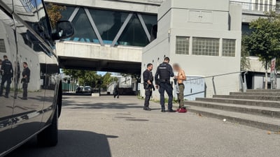 Zwei Polizisten sprechen mit einem Mann auf einer Strasse vor einem Gebäude.
