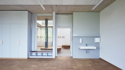 Klassenzimmer mit Holzboden, Spülbecken und einem Fenster zum Gang.