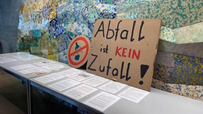 Plakat mit Aufschrift 'Abfall ist kein Zufall' neben Infotisch.",