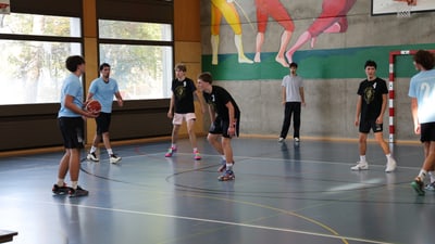Jugendliche spielen Basketball in Sporthalle.