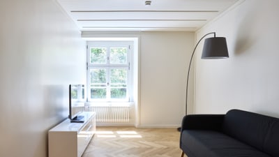 Wohnzimmer mit schwarzem Sofa, Stehlampe und TV.