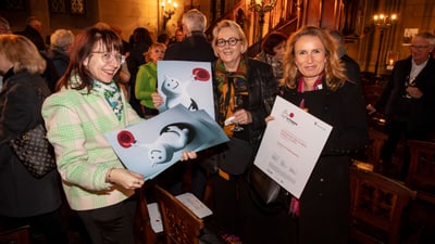 Frauen halten Kunstplakate in einem Raum mit Publikum.