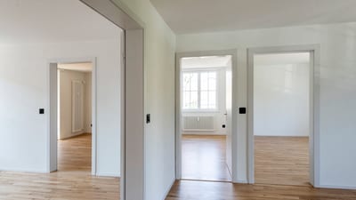 Innenansicht eines leeren, mehrtürigen Raumes mit Holzboden.