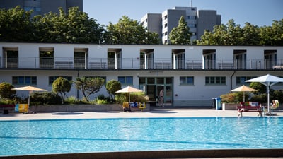 Aussenansicht eines Schwimmbads mit Gebäuden im Hintergrund.