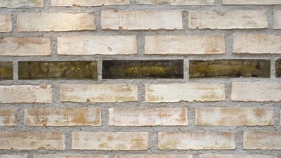 Steinmauer in der eine Steinreihe durch grün-braunes Glas ersetzt wurde.