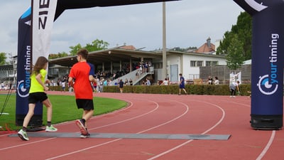 Zwei Läufer unter der Ziellinie des Waldlauf Lange Erlens auf Sportanlage Grendelmatte