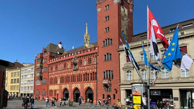 Historisches rotes Gebäude mit Turm und Flaggen auf einem belebten Platz.