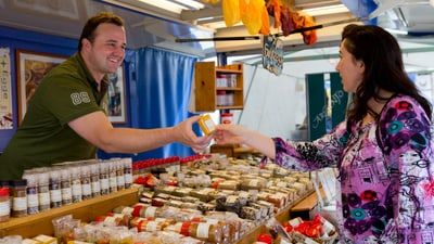 Gewürzverkäufer reicht der Kundin ein Produkt.