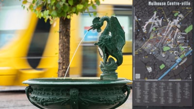 Drachenbrunnen vor Stadtplan in Mulhouse, vorbeifahrende gelbe Strassenbahn.