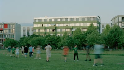 Menschen auf Rasen vor Wohngebäuden.