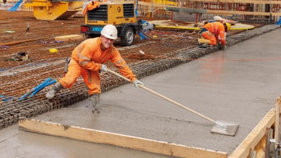 Bauarbeiter glättet Beton auf Baustelle.",