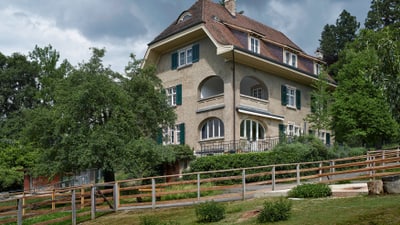 Historisches Haus mit Garten und bewölktem Himmel.