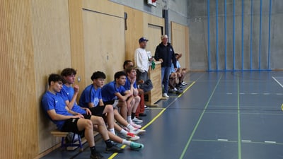 Basketballteam auf der Bank in der Sporthalle sitzend.