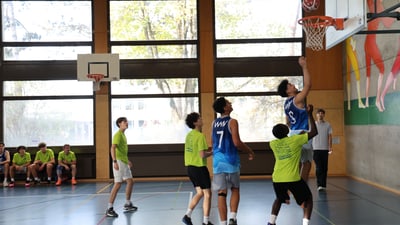 Jugendliche spielen Basketball in einer Turnhalle.