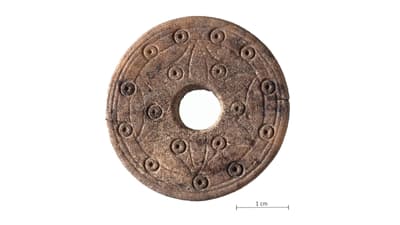 Runder Spinnwirtel aus Knochen und mit geometrischen Mustern sowie Massstab 1 cm.