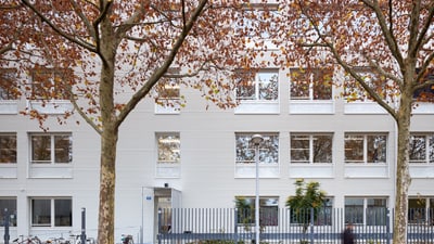 Weisse Wohngebäude hinter Herbstbäumen und gehender Person.