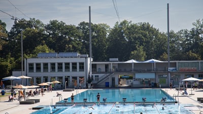 Freibad mit Schwimmern und Gebäuden im Hintergrund.