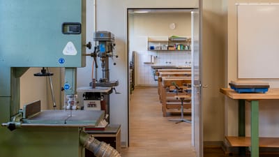 Werkstatt mit Maschinen und offenen Tür zum Klassenzimmer mit Bänken.