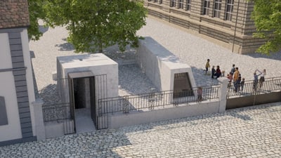 Gedenkstätte mit Baum und Besuchergruppe neben historischem Gebäude.