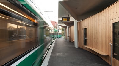 Holzgebäude mit Vordach und einer Anzeigetafel daneben ein grünes Tram.