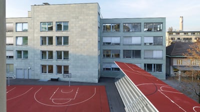 Moderne Schulgebäude mit rotem Sportplatz im Vordergrund.