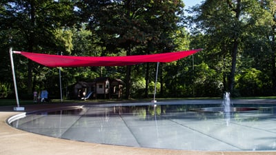 Kleiner Pavillon mit rotem Sonnensegel über Wasserbecken im Park.