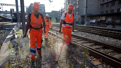 Bahnarbeiter in orangen Sicherheitswesten gehen entlang der Gleise.