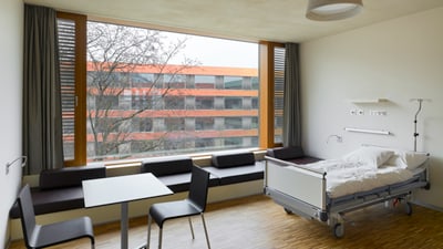 Modernes Krankenhauszimmer mit grossem Fenster und Bett.