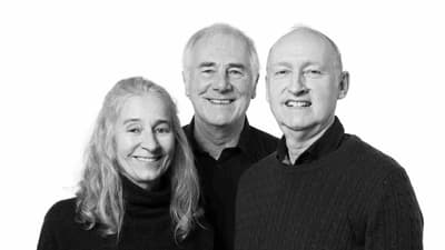 Drei lächelnde Personen in Schwarz-Weiss-Porträt.