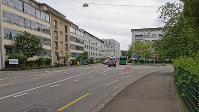 Städtische Strasse mit Gebäuden und Autos bei bewölktem Himmel.